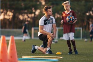 Trener tłumaczy ćwiczenie piłkarskie chłopcu